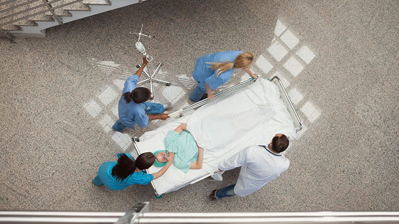 Three nurses and one doctor pushing one patient in a bed in hospital corridor