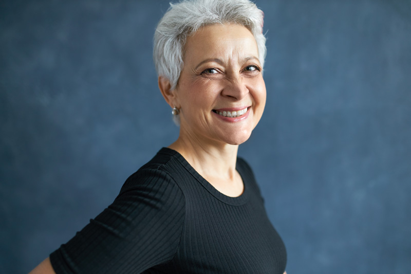 half profile image of cheerful attractive middle aged woman with short gray hair and wrinkles having fun laughing at joke smiling broadly at camera