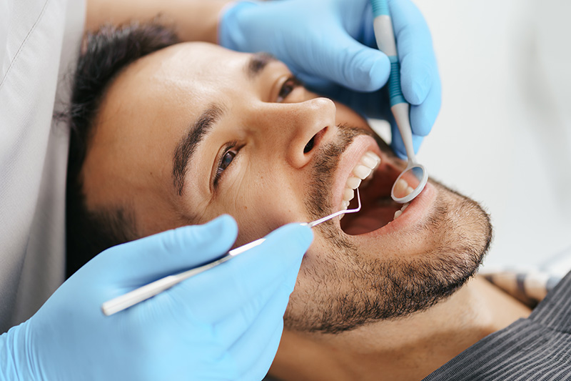 sonriente joven sentado silla dentista mientras medico examina sus dientes